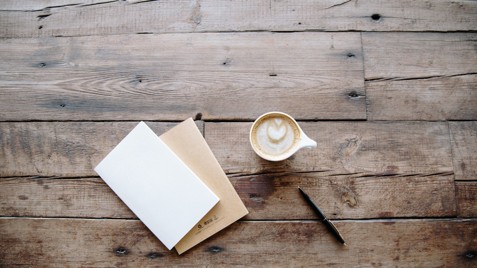 Notebooks, a pen, and coffee on a work surface.